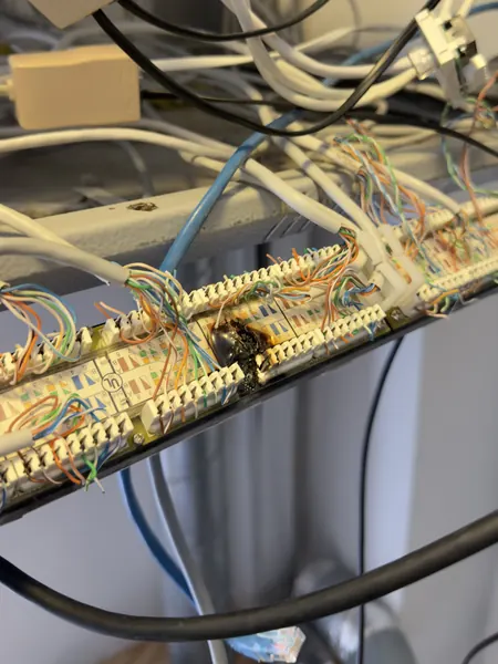 Close up of a panel where network cables are terminated, with a burnt, blackened patch on it and cables tangled around it