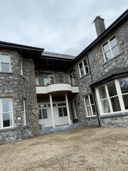 Front of a large stone house in Galway, with a curved balcony over the entrance, a bay window and a gravel drive