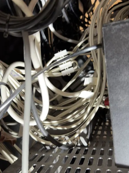 Tangled white, grey and black cables on a perforated shelf behind the old rack