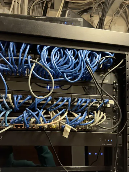 Front of the original rack before the rescue, with blue patch leads heaped over the network switches, loose power cables hanging down and a Control4 CORE 5 controller below the switches