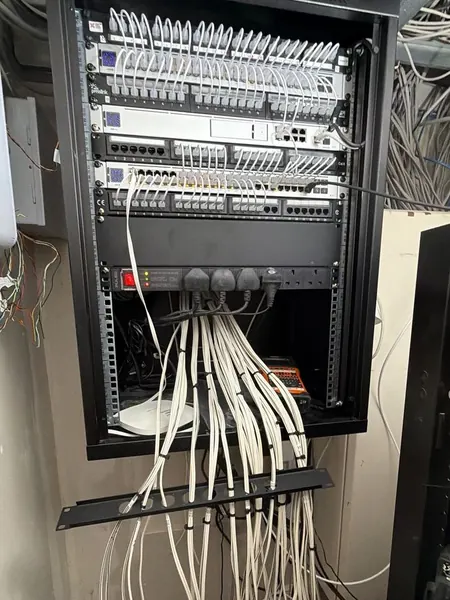 Wall mounted cabinet being rebuilt, with patch panels, white network switches joined by short white patch leads, a rack power strip and long cables tied in groups through a cable management bar