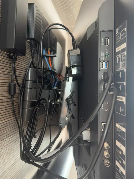 Rear of a wall mounted TV showing HDMI, USB, network and aerial sockets, with a loop of black cable and a tangle of power and network leads on the bracket