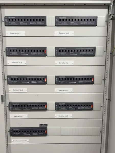 Open lighting cabinet with eight Philips Dynalite relay controllers labelled Switcher No.1 to No.8 and a miscellaneous controller below them