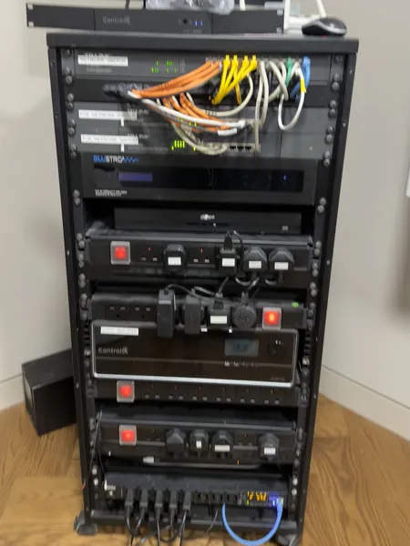 Equipment rack with network switches, orange, yellow and white patch leads bundled over the front, a Blustream unit, Control4 equipment and rack power strips