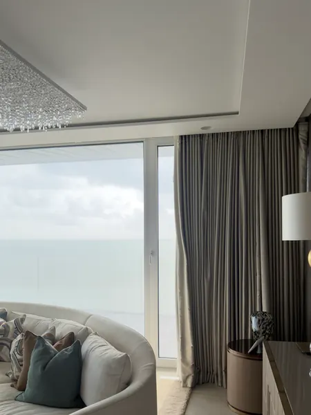 Room in the Cork house with a curved cream sofa in front of large windows with a view of the sea, and a floor length curtain at the right