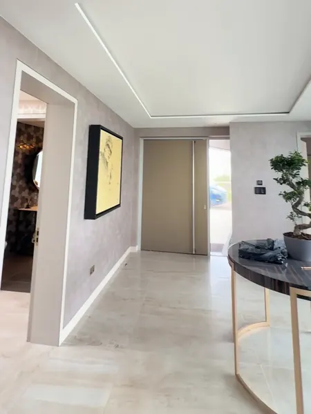 Hallway of the Cork house at the final site survey for the Control4 to Crestron Home project, with a framed yellow picture on a pale wall, a tan door at the far end and a round table with a potted tree