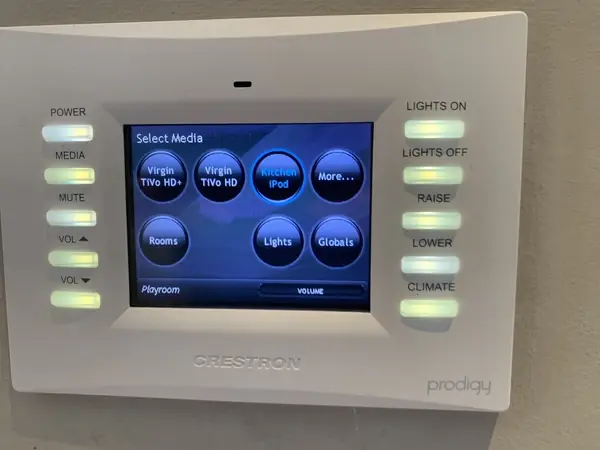 Older Crestron Prodigy touch panel on a wall, showing a Select Media menu with TV, music, rooms and lights
