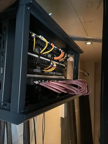 Second, wall mounted rack with patch panels, yellow and orange patch leads and pink speaker cables