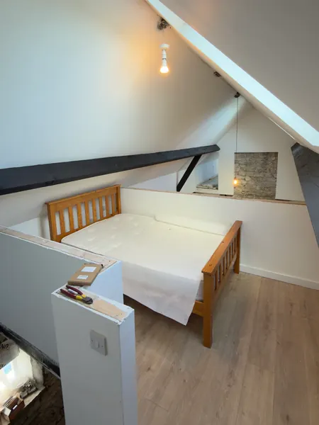 The finished bedroom in the roof space with a timber bed, white sloping ceilings and a roof window