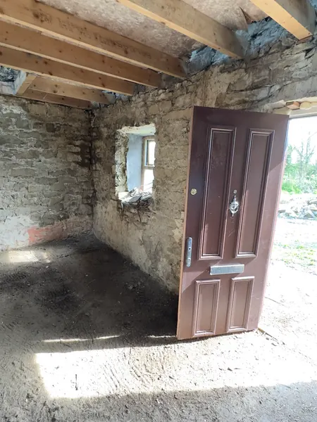 The cottage stripped back to a bare stone shell with new ceiling joists and the front door open to the yard