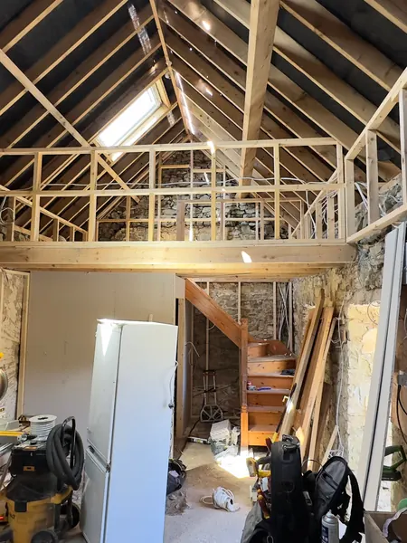 Stud walls, roof insulation and a new timber staircase inside the cottage during first fix, with tools on the floor