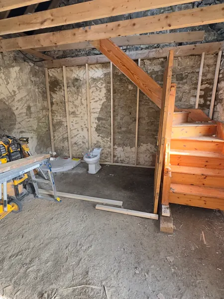 Timber stud frame against the old stone wall of the cottage with a new staircase and a toilet pan waiting to be fitted