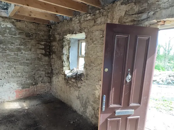 The stripped stone shell of Ivy Cottage in Roscommon with the front door open to the yard and new joists overhead
