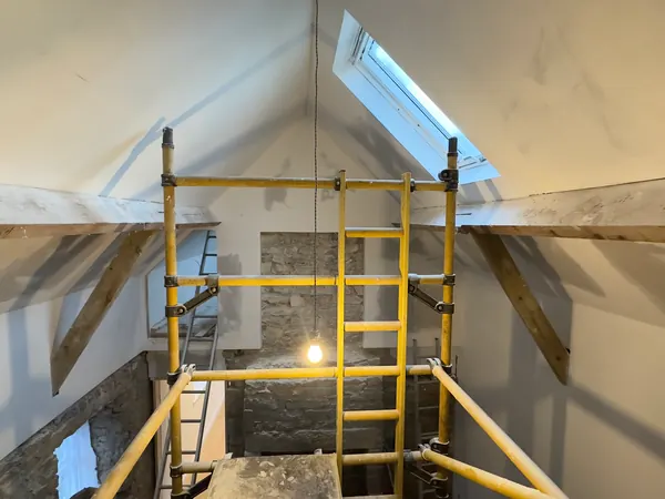 The vaulted ceiling at Ivy Cottage in Roscommon being painted white from a yellow scaffold tower, with the old beams and two roof windows
