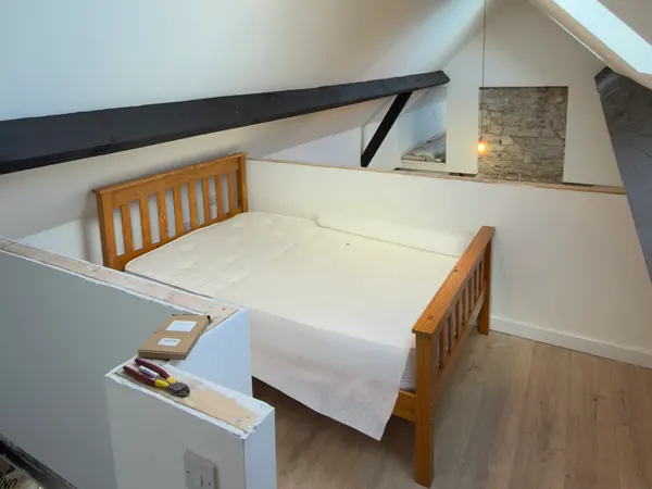 The bedroom under the eaves at Ivy Cottage in Roscommon, a timber bed under white sloping ceilings with a black painted beam and a roof window