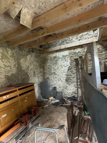 Bare stone walls and old timber joists inside the derelict cottage, with debris on the floor