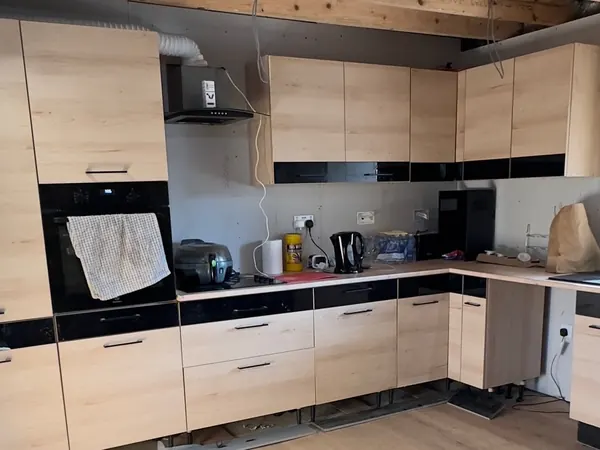 The finished kitchen with light oak units, black worktop panels, a built in oven and a window over the sink