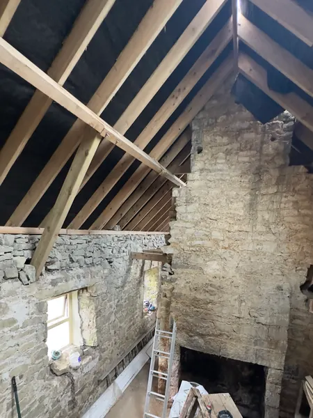 Open roof timbers and a stone gable inside the derelict cottage, daylight coming through the rafters