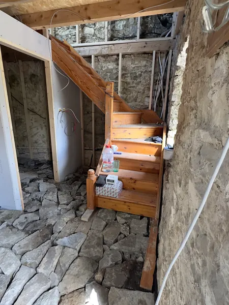 The timber staircase beside the exposed stone wall, with the old flagstones still on the floor
