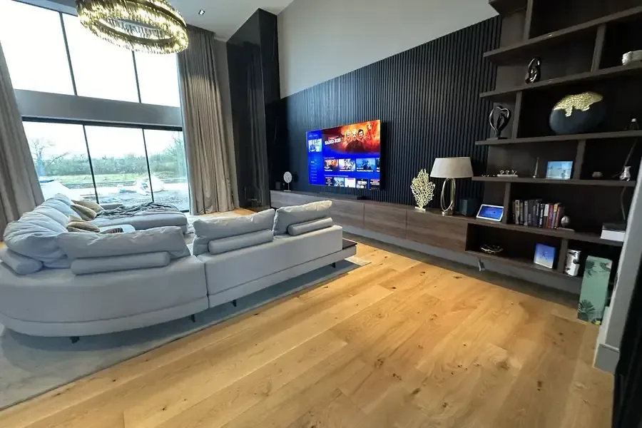 A wall mounted TV above a low media unit in a family room with a curved sofa and oak floor, the kind of job the TV wall mounting cost covers