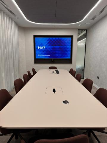 Long white boardroom table facing a wall display with a camera below it