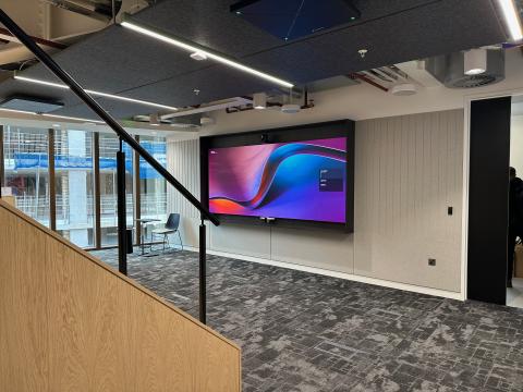 A large screen and video bar on a panelled wall, seen past an oak staircase