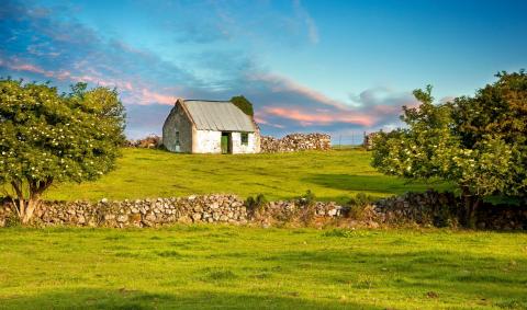 A small stone cottage in a green field bordered by dry stone walls