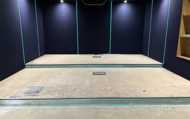 A cinema room under construction: dark fabric walls, upright strips of light and a stepped concrete floor
