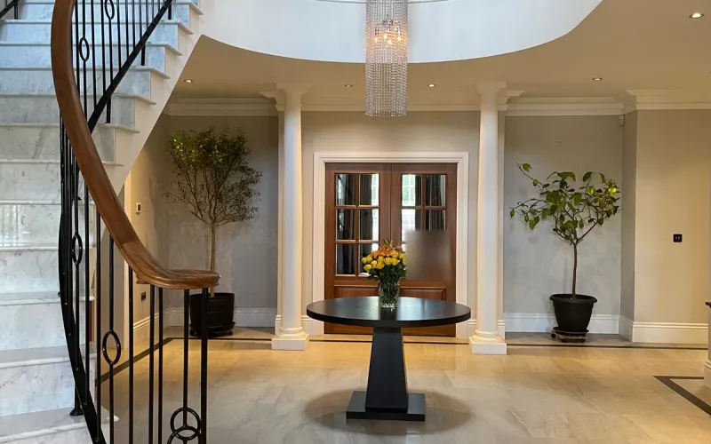A house run by Crestron home automation: a sweeping marble staircase with an iron balustrade below a long crystal chandelier
