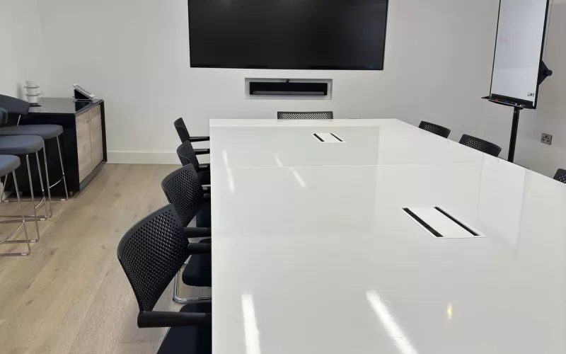 Meeting room wall display with a Sonos soundbar in a recess below it, above a long white table and black chairs in a Dublin office