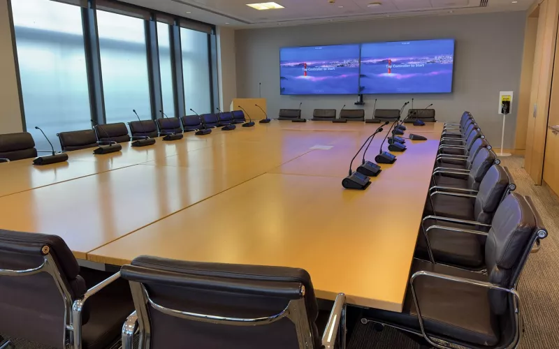 Boardroom audio system in Dublin city centre, with conference microphones along both sides of the timber table and Zoom Rooms on the twin screens at the far end