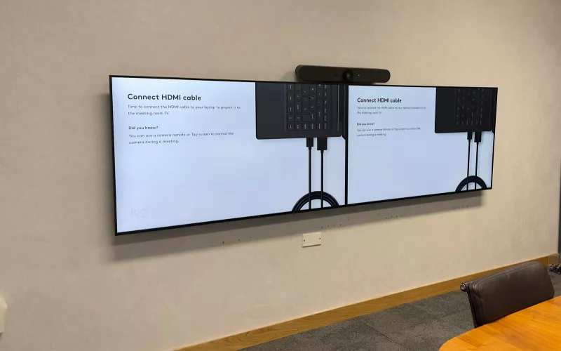 Meeting room technology in a Dublin city centre office: twin screens side by side with a Logitech video bar above them, beside an oval timber table