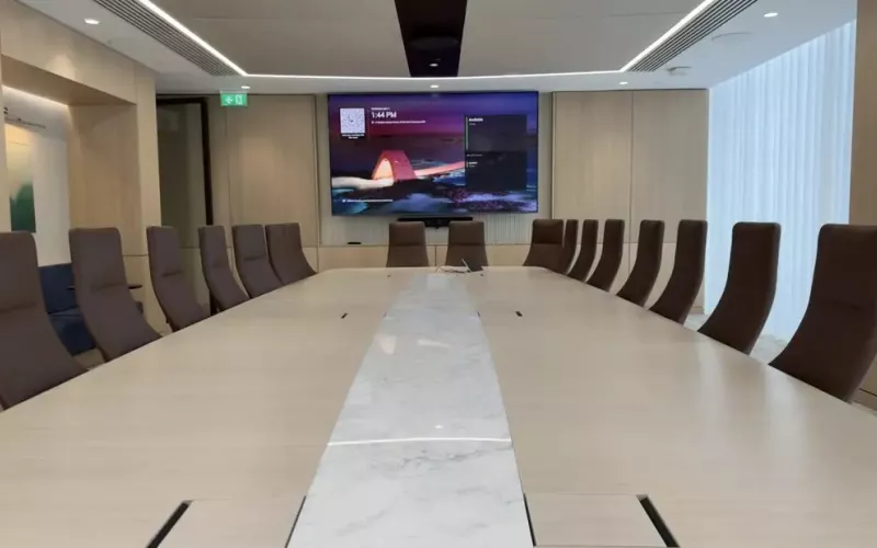 Timber panelled boardroom with a long table, brown leather chairs and a wall display with a video bar beneath it, a room of the sort Jabra Reach is designed to serve