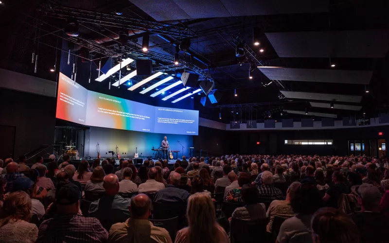 Full congregation at River Valley Church facing a speaker on stage under a wide angled LED wall, with Biamp church audio from Community LVH-900 horns on the truss overhead