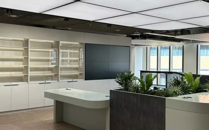 Open plan office area with lit display shelving, a video wall, planting and large windows, an example of the shared space whose use a Logitech Spot room sensor is built to measure