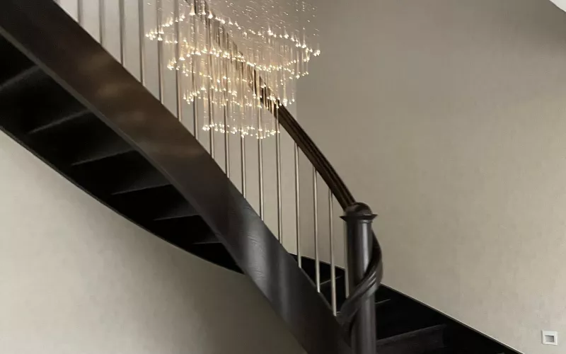 Curved dark oak staircase lit by a cascading fibre optic chandelier, with a step light set into the wall