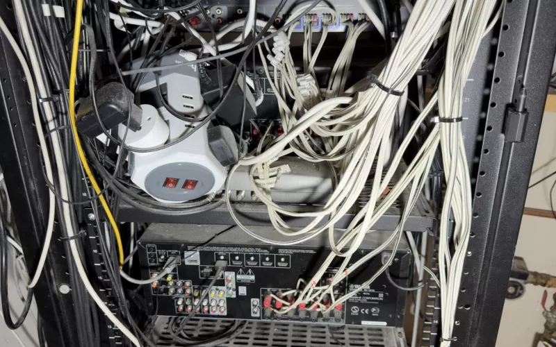 Control4 rescue in Cork: the back of an overloaded equipment rack, with power adaptors, a multi way power unit, an AV receiver and bundles of white cable
