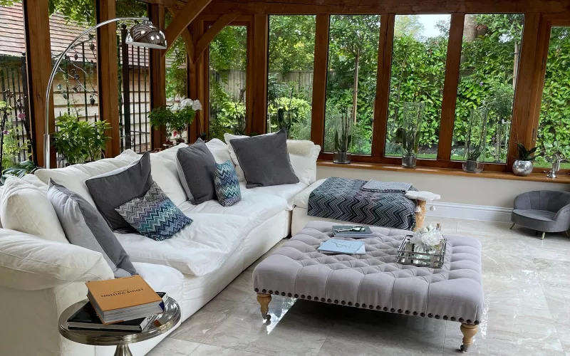 Oak framed garden room with a white corner sofa, a tufted ottoman and a marble floor, the kind of room Wi-Fi access points in the main house often fail to reach