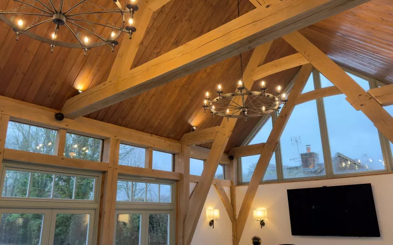 Oak framed room with two wrought iron chandeliers, uplit beams and wall lights beside the TV, layers of light that Lutron or Rako can set in one scene