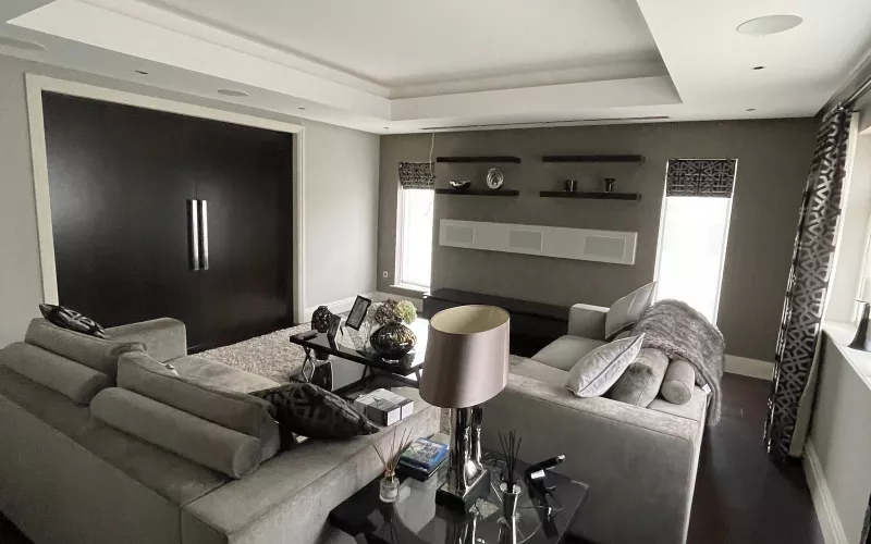 Grey sitting room with two sofas, ceiling speakers in a lit coffer and a slim white soundbar under floating shelves, a typical room for a Crestron Cevo Mini Remote