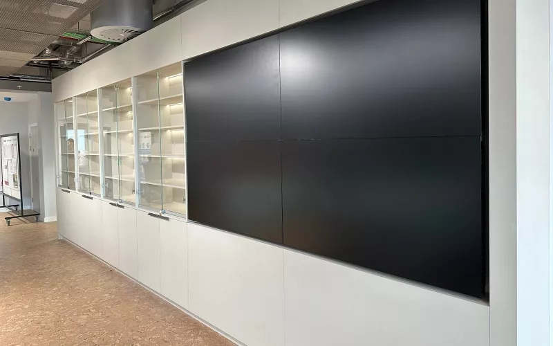 Four panel video wall built into white office joinery beside lit display cabinets, a layout a DM NVX 370 system can drive
