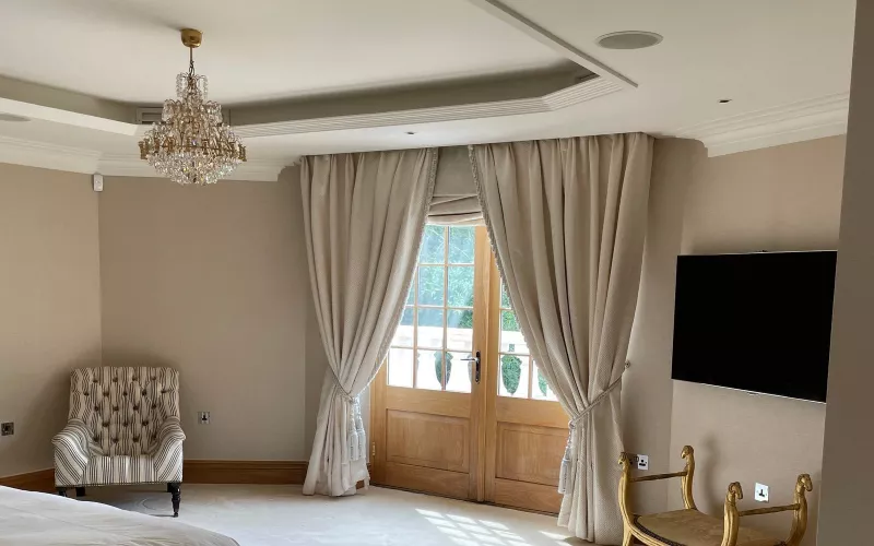 Bedroom with a crystal chandelier, a ceiling speaker, full length curtains and a wall mounted TV: lighting, shading and audio, the areas Crestron updated around CEDIA Expo 2026