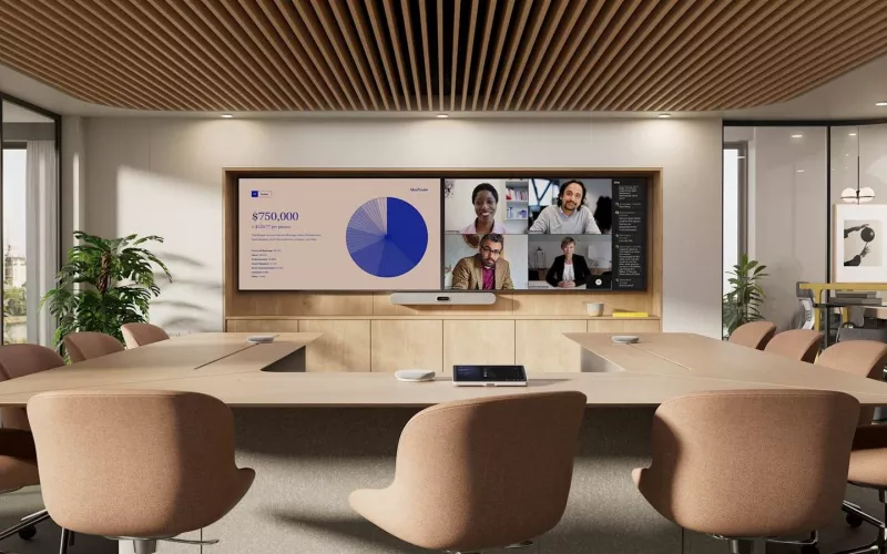 Off-white Logitech Rally Bar 2 mounted below two wall displays in a meeting room with timber joinery, with round pods and a touch controller on a large conference table