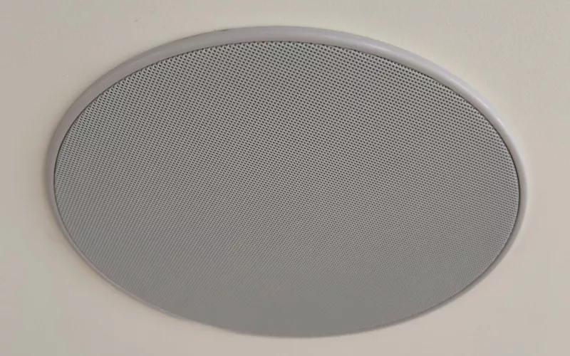 Round white ceiling speaker with a fine mesh grille fitted flush into a smooth plastered ceiling, the neat finish ceiling speakers should have