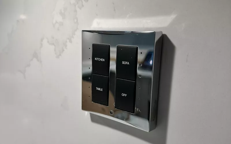 Polished chrome keypad on a white marble kitchen wall with engraved buttons for kitchen, sofa, table and off, the finished end of good smart home wiring