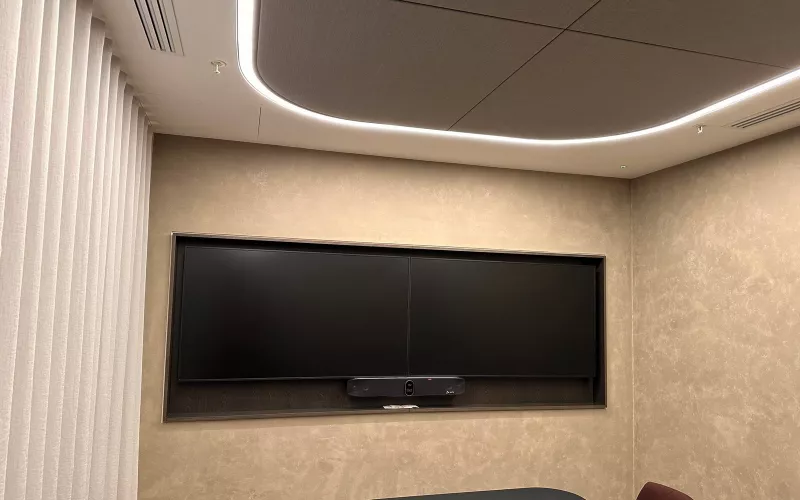Meeting room with two screens set into a lined recess and a video bar below them for Microsoft Teams Rooms calls, under a softly lit ceiling raft