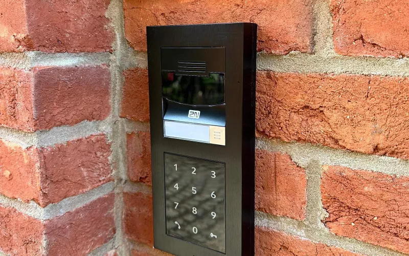 2N video intercom with a camera, call button and keypad set into a brick wall, the kind of gate entry that electric gate wiring has to plan for