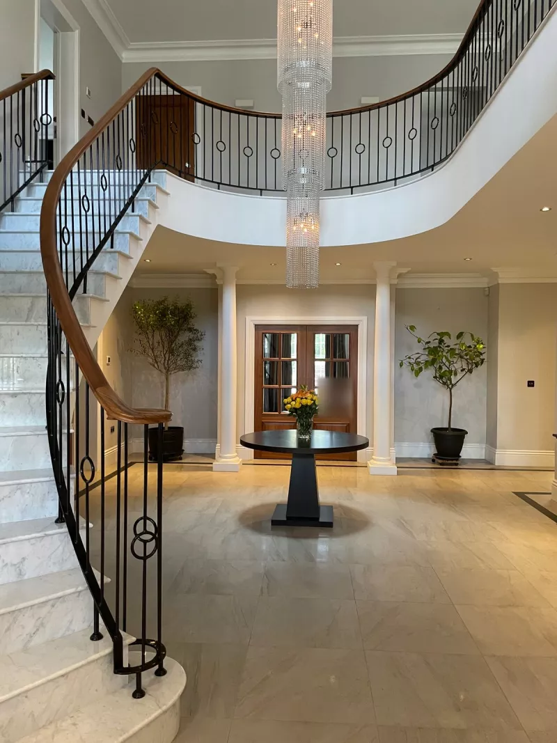 A house run by Crestron home automation: a sweeping marble staircase with an iron balustrade below a long crystal chandelier