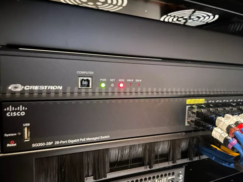 A Crestron control processor on top of a Cisco SG350-28P PoE switch, its ports filled with colour coded patch leads