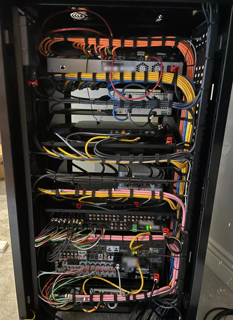 The back of the rack: orange, yellow, blue and pink cable runs strapped in bundles around the Cisco switch, a Sonos unit, a Crestron audio unit and an AV receiver